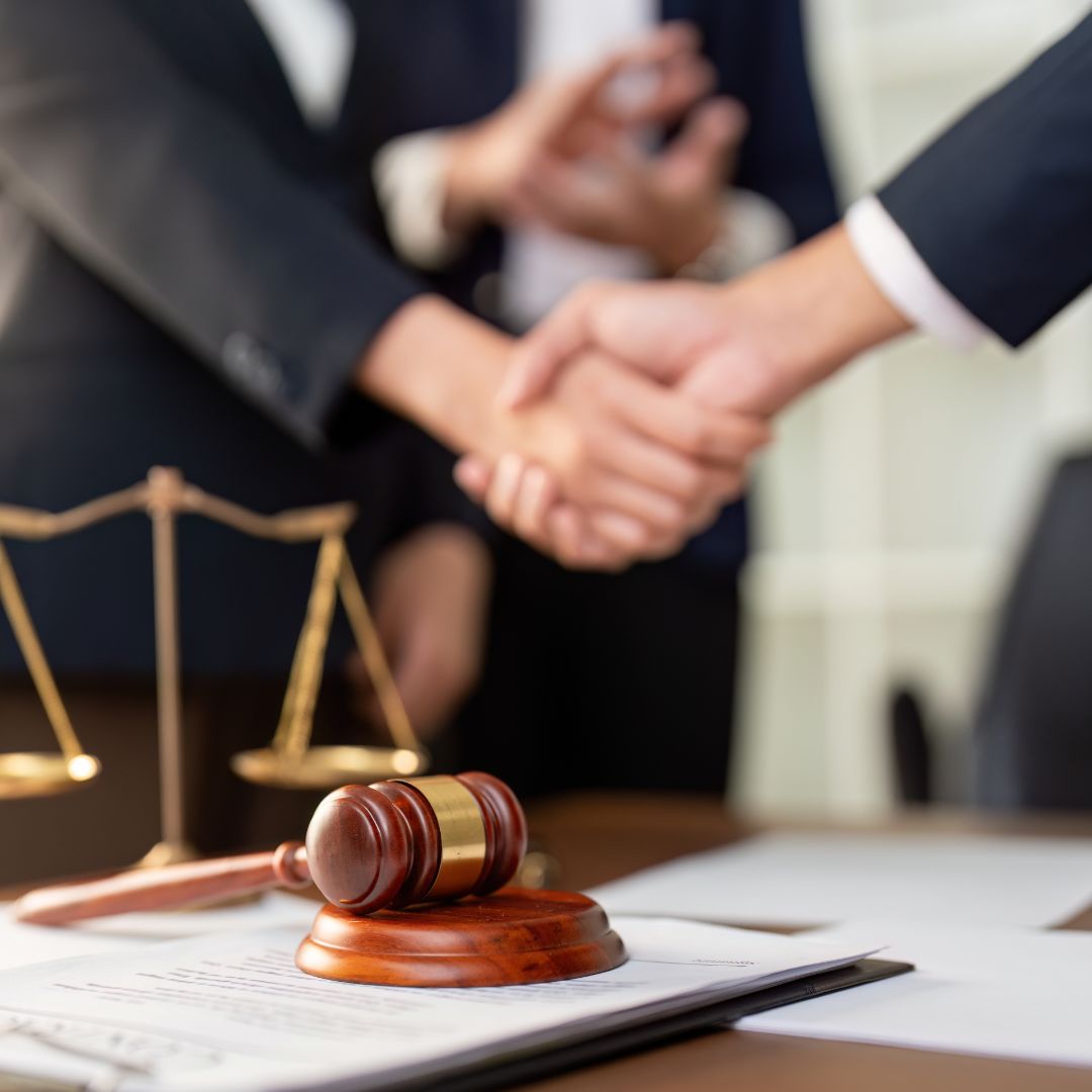 Two people shaking hands across a desk in a law office after discussing a legal matter